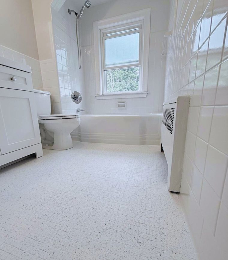 The same bathroom after refinishing, with a bright white tub, tile and floor