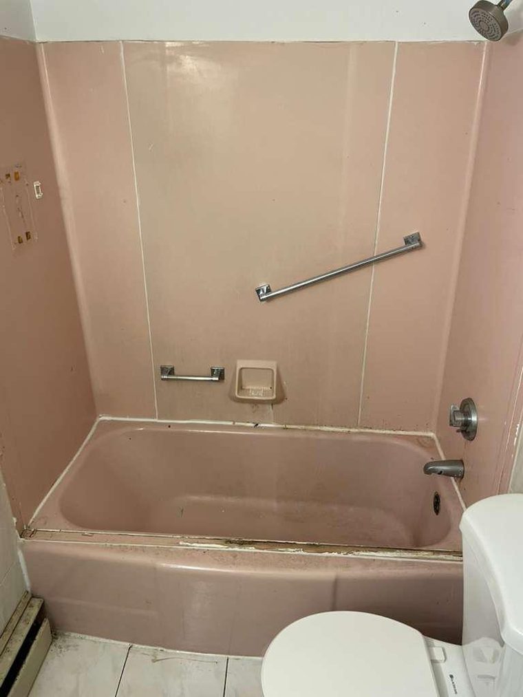 Dated pink fiberglass tub and wall surround with worn caulk before refinishing